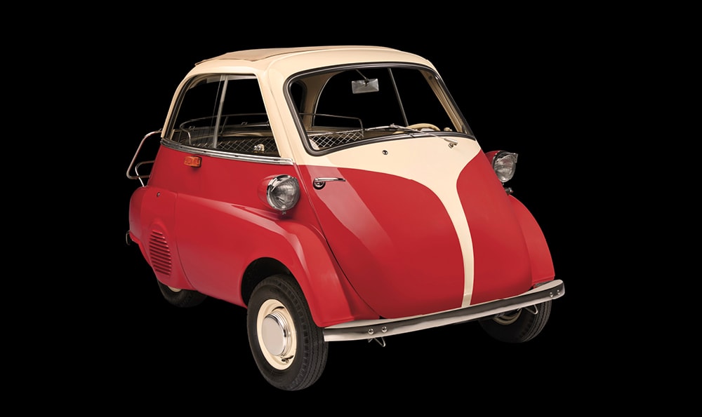 Ein klassisches Mikroauto, ein BMW Isetta, mit roter Karosserie und weißen Akzenten. Es hat eine nach vorne öffnende Tür und kleine runde Scheinwerfer.