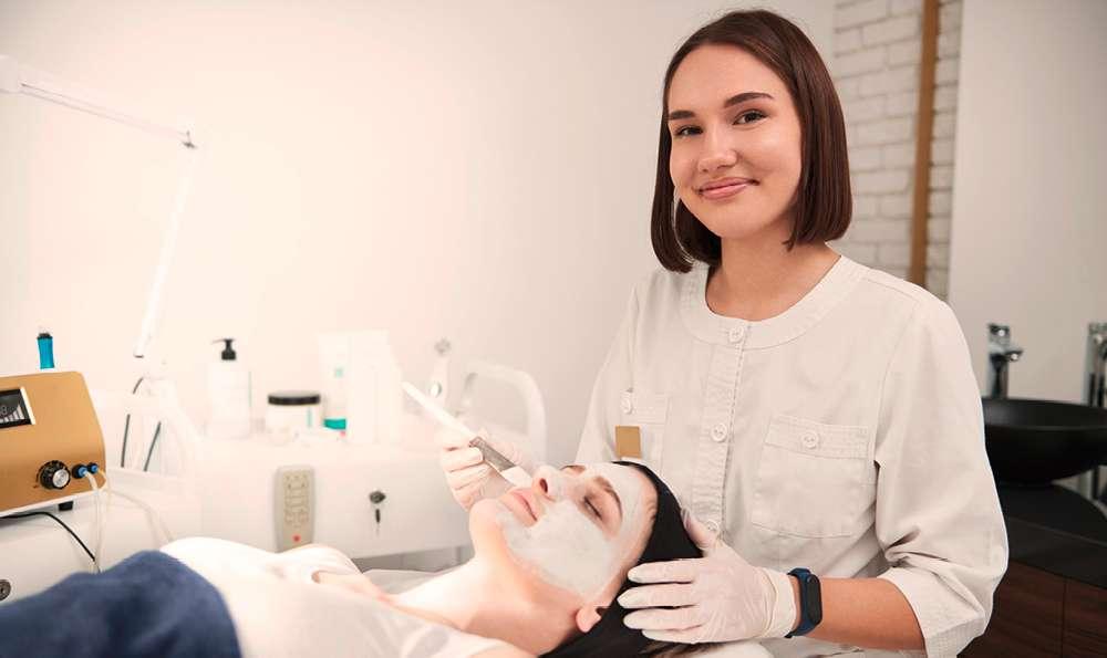 Eine Person in einem weißen Kittel und Handschuhen führt eine Fußbehandlung durch. Im Hintergrund sind verschiedene medizinische oder Spa-Geräte zu sehen.