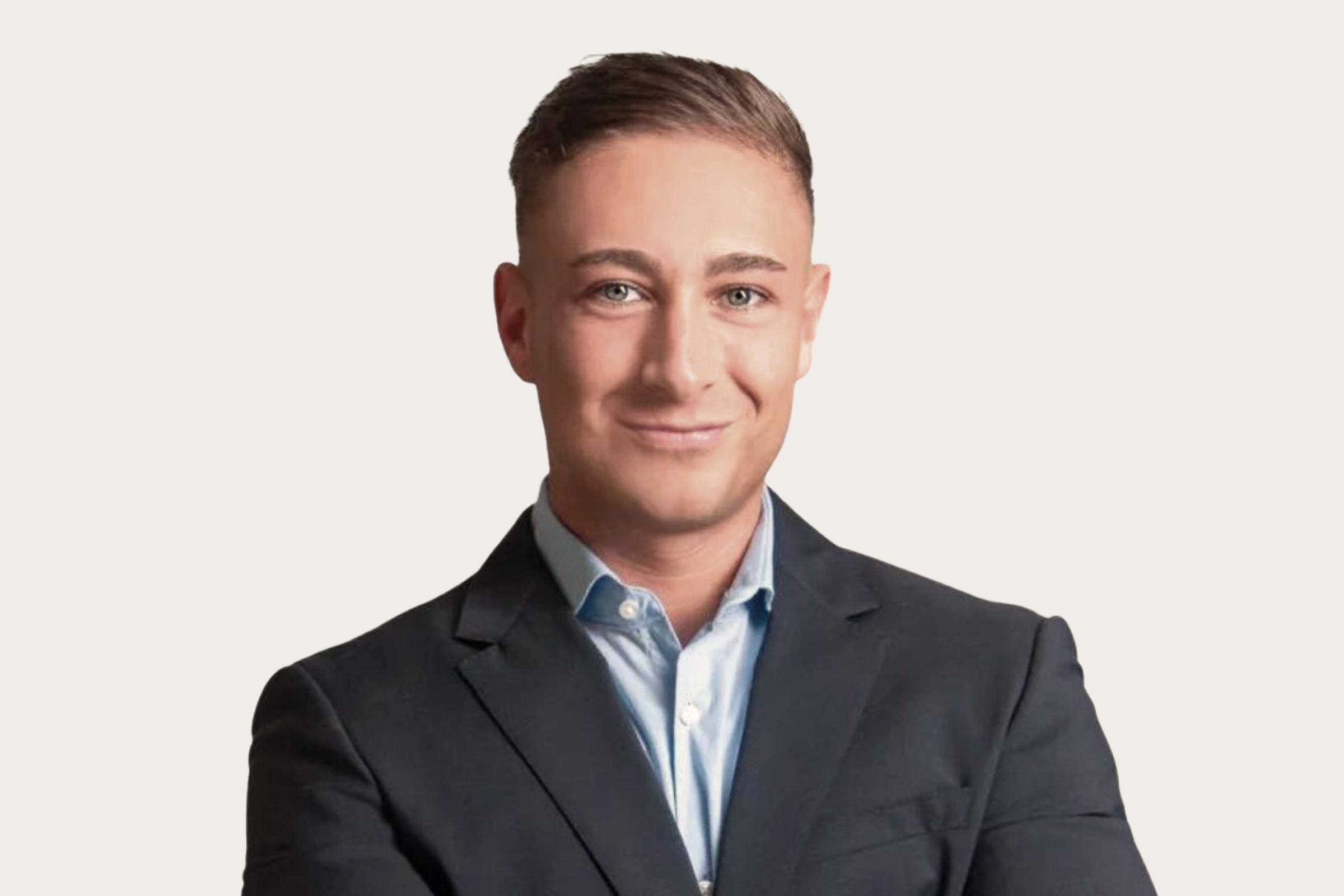 Ein Mann in einem dunklen Anzug und einem hellblauen Hemd vor einem neutralen Hintergrund.