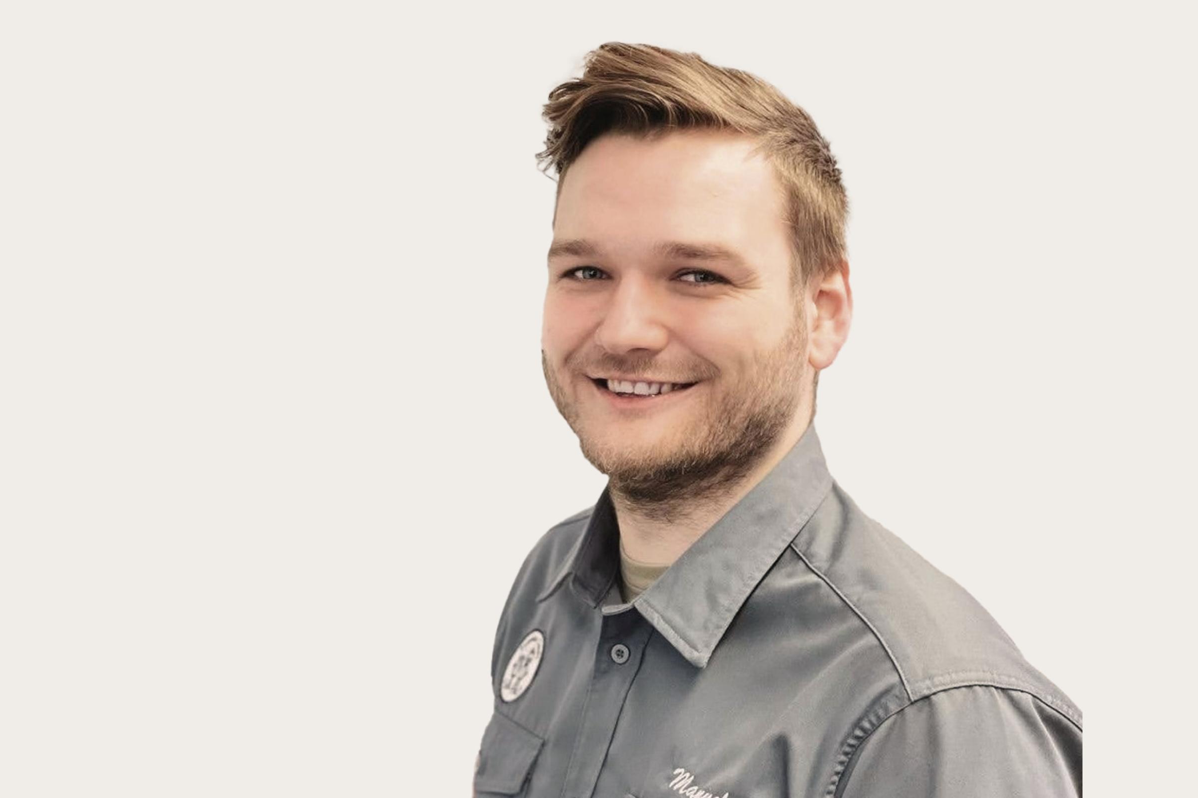 Ein Mann in einer grauen Uniform mit einem Abzeichen auf der linken Brustseite.