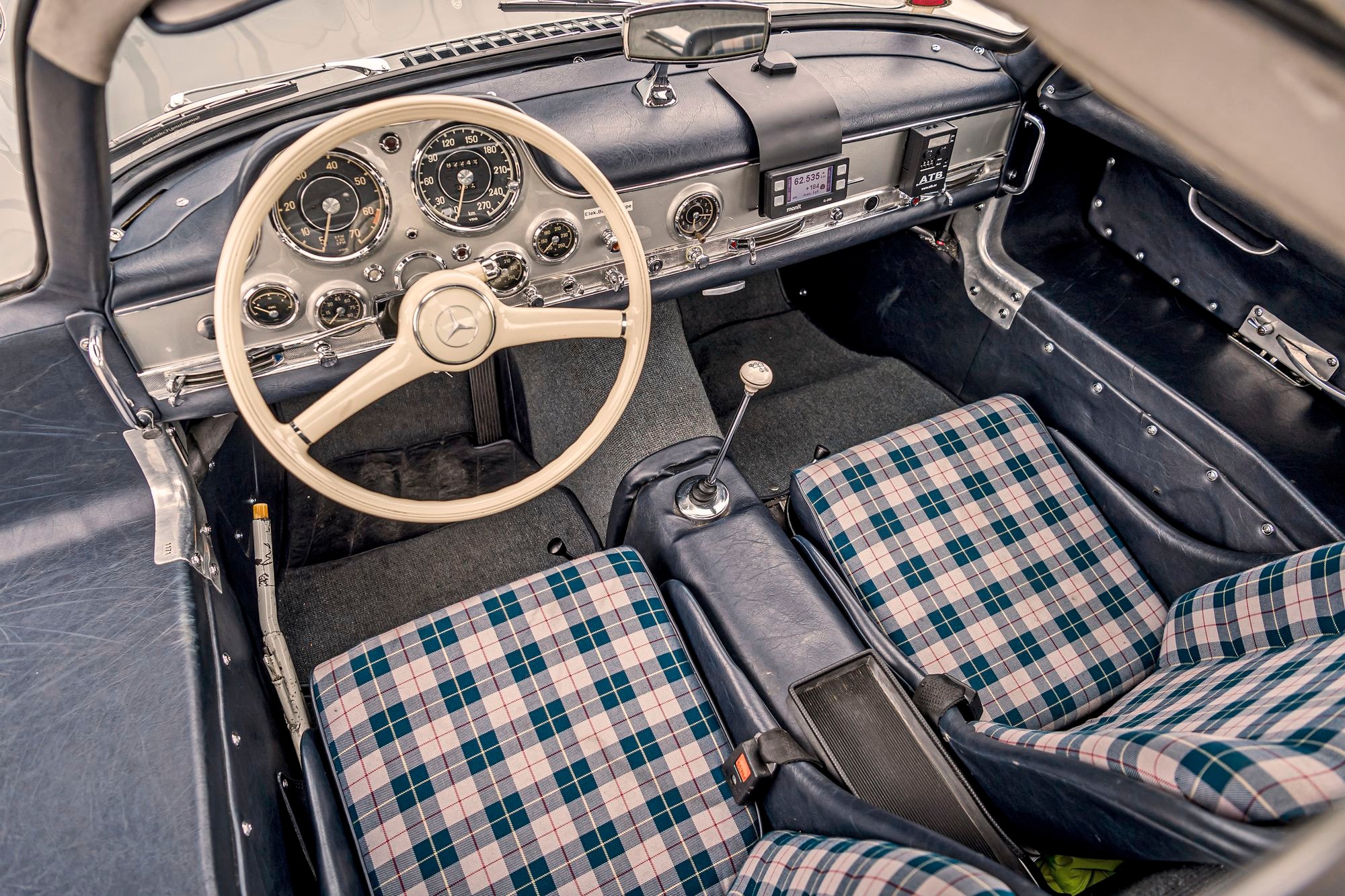 Vorderer Innenraum des mercedes Benz 300 SL mit Blick auf die karierten Vordersitze und das weiße Lenkrad