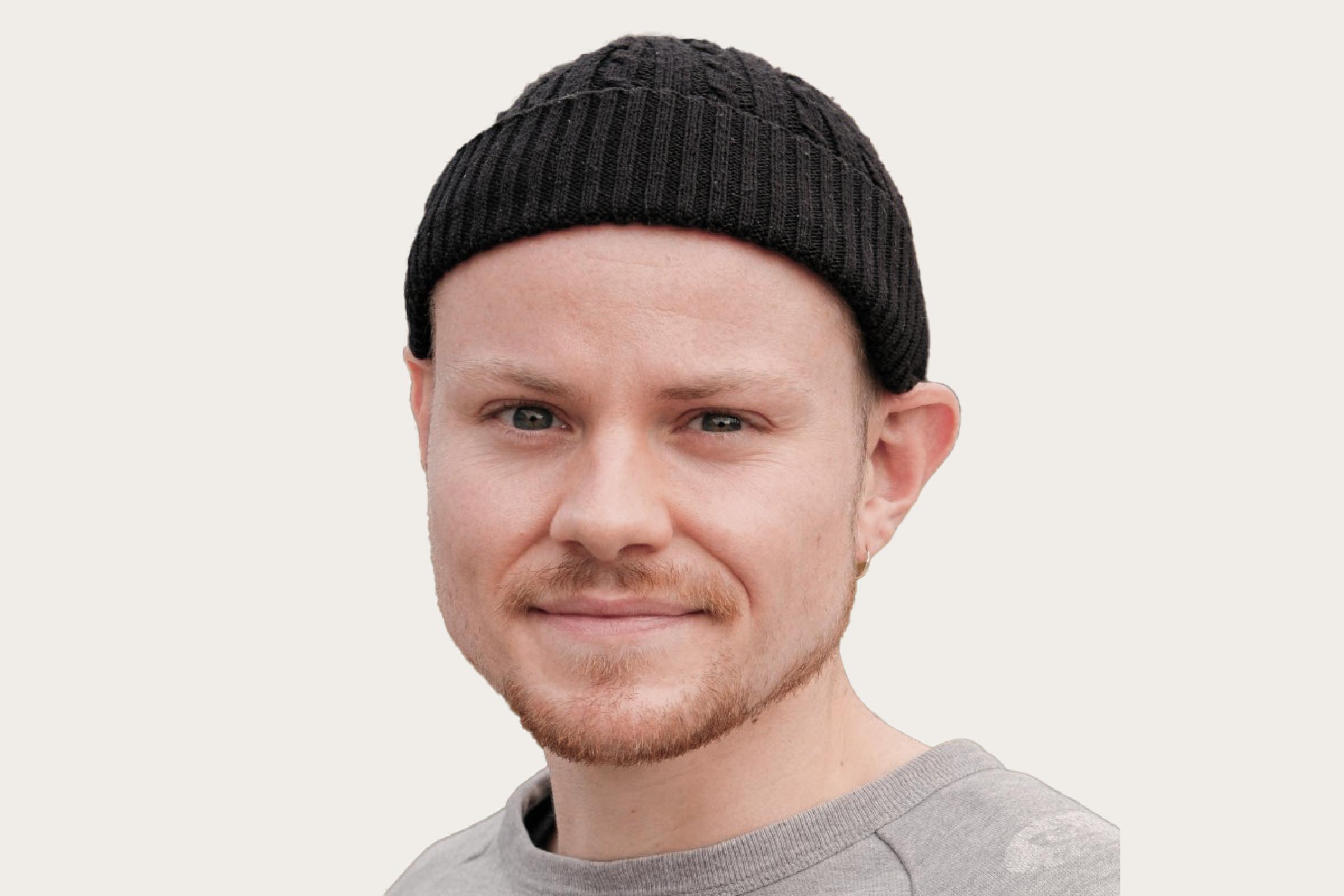 Nick Oestreich, ein Gastautor bei Hiscox, trägt eine schwarze Strickmütze und ein graues Shirt.