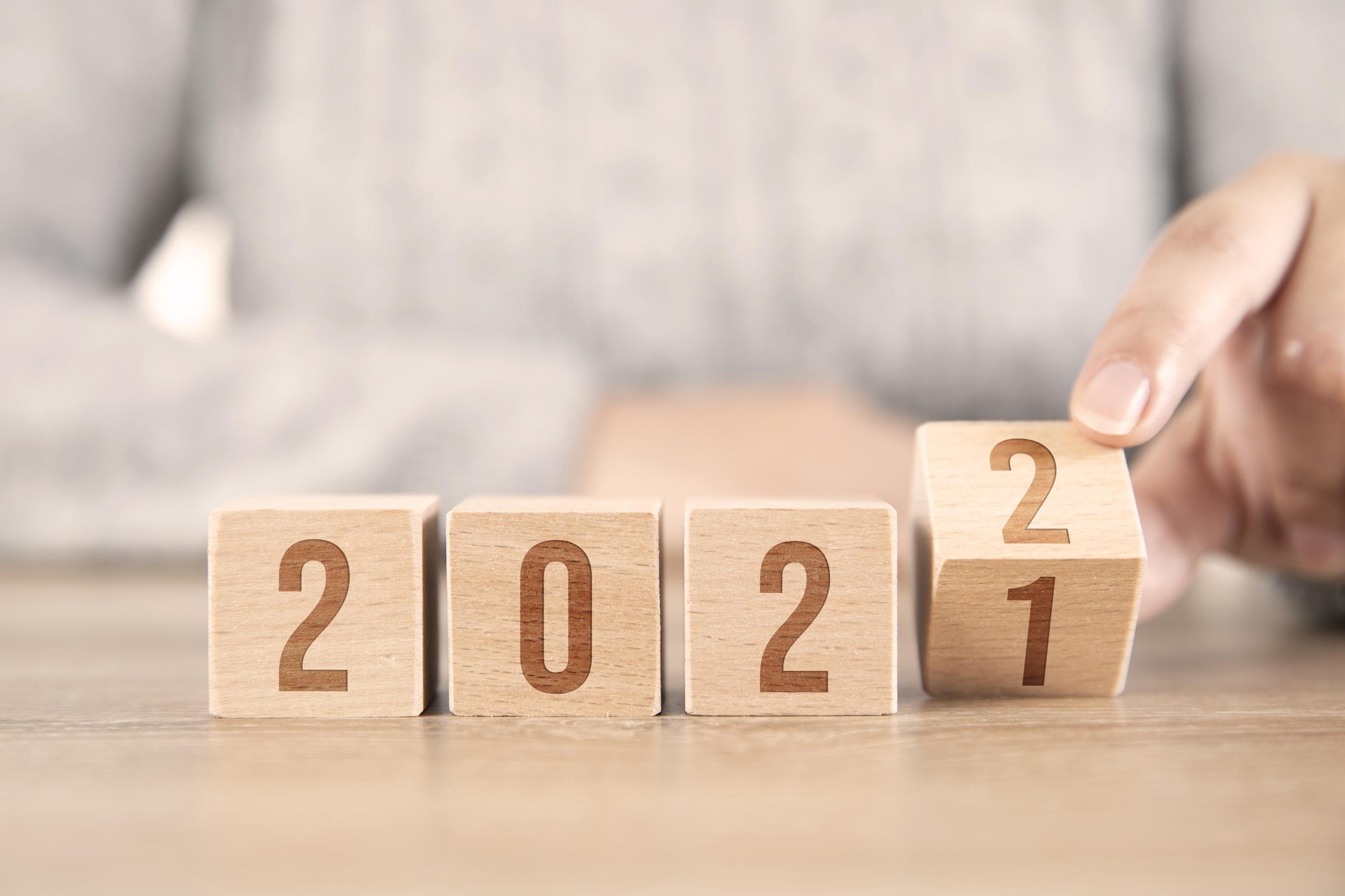 Vier Holzblöcke zeigen die Zahlen "2021". Eine Hand dreht den letzten Block, um die Zahl "1" in "2" zu ändern, was den Übergang von 2021 zu 2022 symbolisiert.