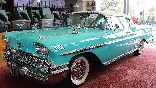 Ein klassischer türkis-weißer Chevrolet Bel Air aus den 1950er oder 1960er Jahren, der auf einem roten Teppich in einem Innenraum ausgestellt ist.