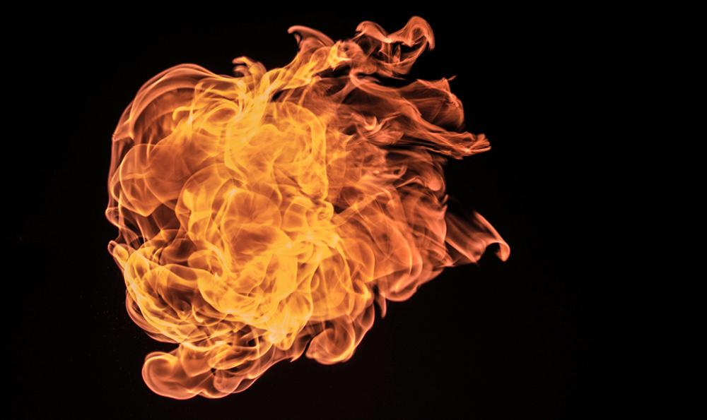 Ein dynamisches und komplexes Flammenmuster vor einem schwarzen Hintergrund. Die Flammen wirbeln und kräuseln sich, wobei sie verschiedene Gelb-, Orange- und Rottöne zeigen.