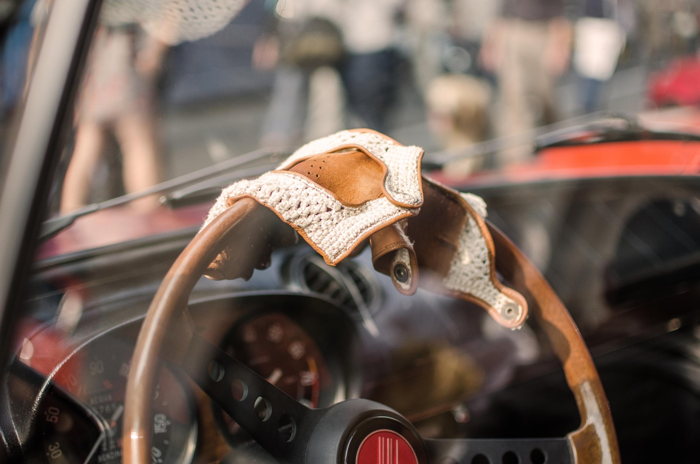 Ein Nahaufnahme des Lenkrads eines klassischen Autos mit darauf drapierten Vintage-Fahrerhandschuhen aus Leder und gehäkeltem Stoff.