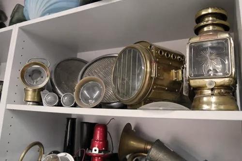 Ein Regal mit verschiedenen alten Schiffsleuchten und Laternen aus Messing. Die Leuchten haben unterschiedliche Größen und Formen und sind auf zwei Regalböden verteilt.