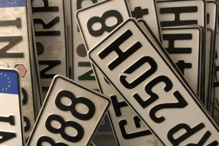 Ein Stapel von Fahrzeugkennzeichen, die sich überlappen. Ein auffälliges Kennzeichen in der Mitte trägt die Aufschrift "P25OSH", ein weiteres sichtbares Kennzeichen lautet "888".