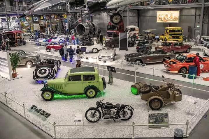Ausstellung von Oldtimern und klassischen Fahrzeugen in einem gut beleuchteten Innenraum.