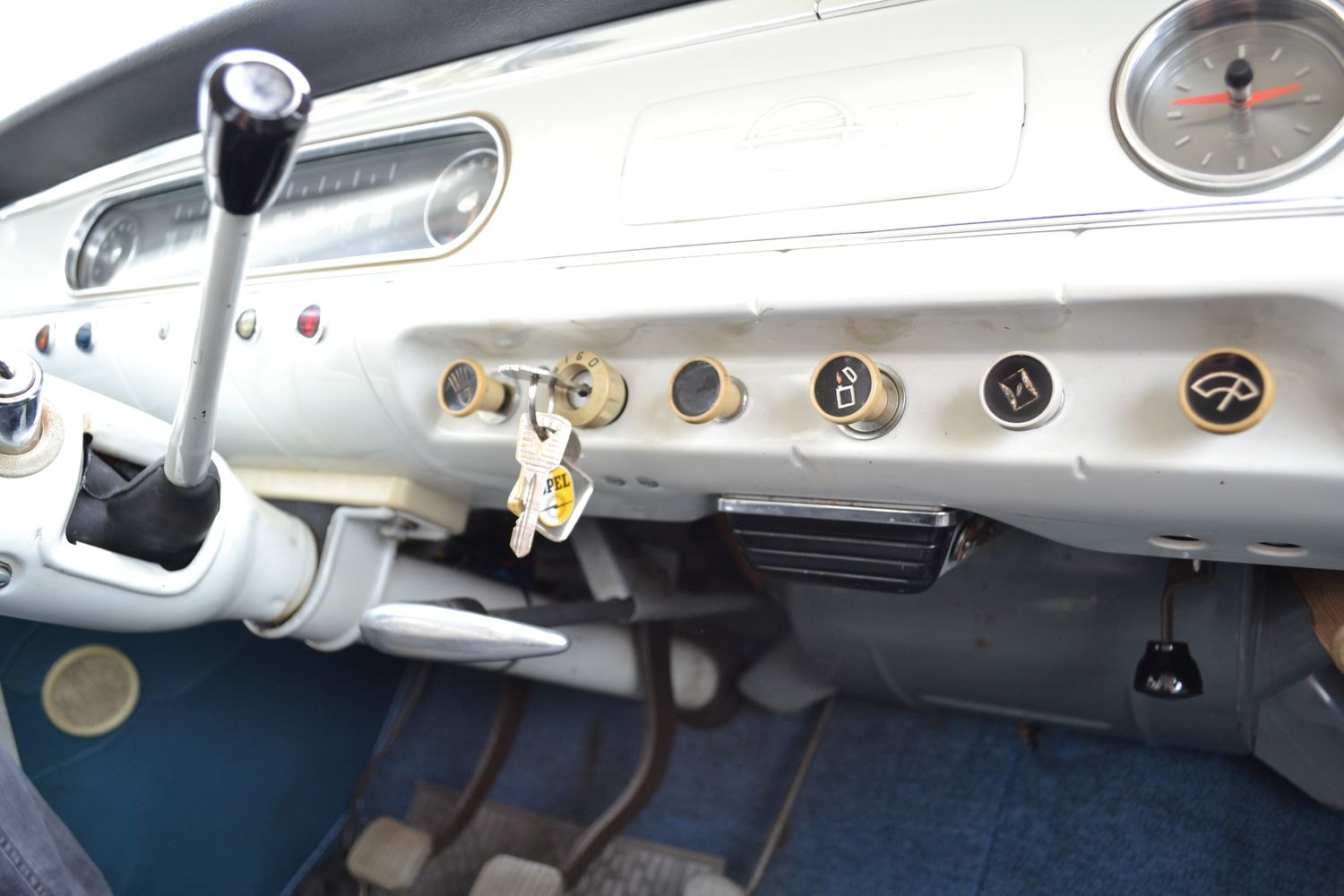 Armaturenbrett eines Oldtimers mit mehreren Bedienknöpfen, einem Zündschlüssel, einem Tachometer und einer Uhr.