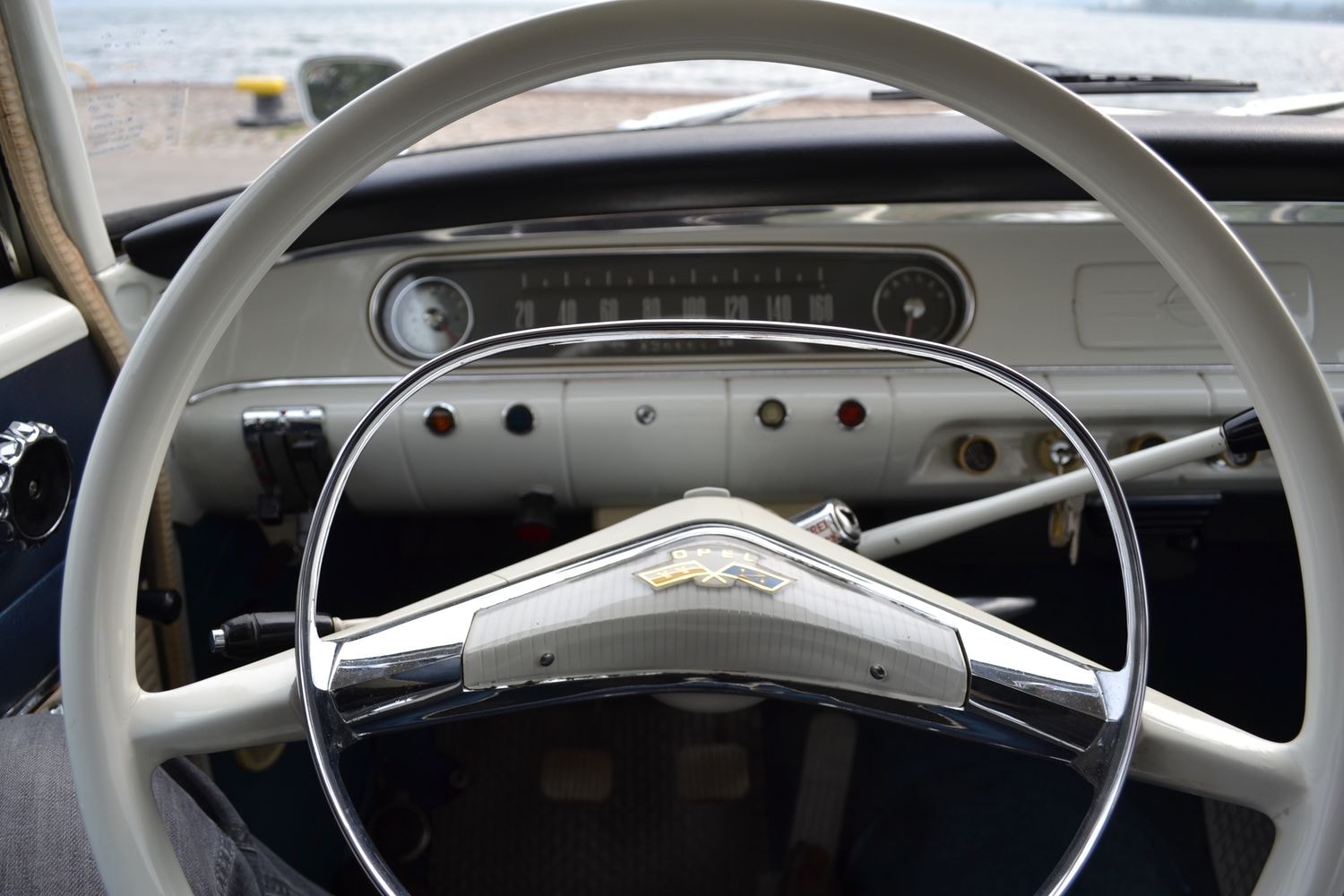 Innenraum eines Oldtimers mit großem Lenkrad, analogem Tachometer und verschiedenen Knöpfen und Schaltern.