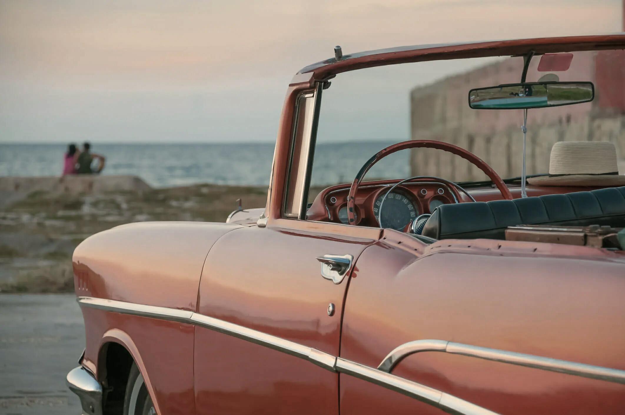 Ein rotes Cabrio, das in der Nähe einer Küste mit dem Ozean im Hintergrund geparkt ist.