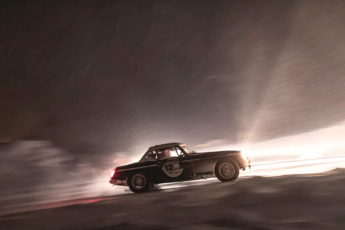 Ein schwarzes Vintage-Sportauto mit der Nummer 12, das mit hoher Geschwindigkeit durch eine verschneite oder vereiste Umgebung fährt.