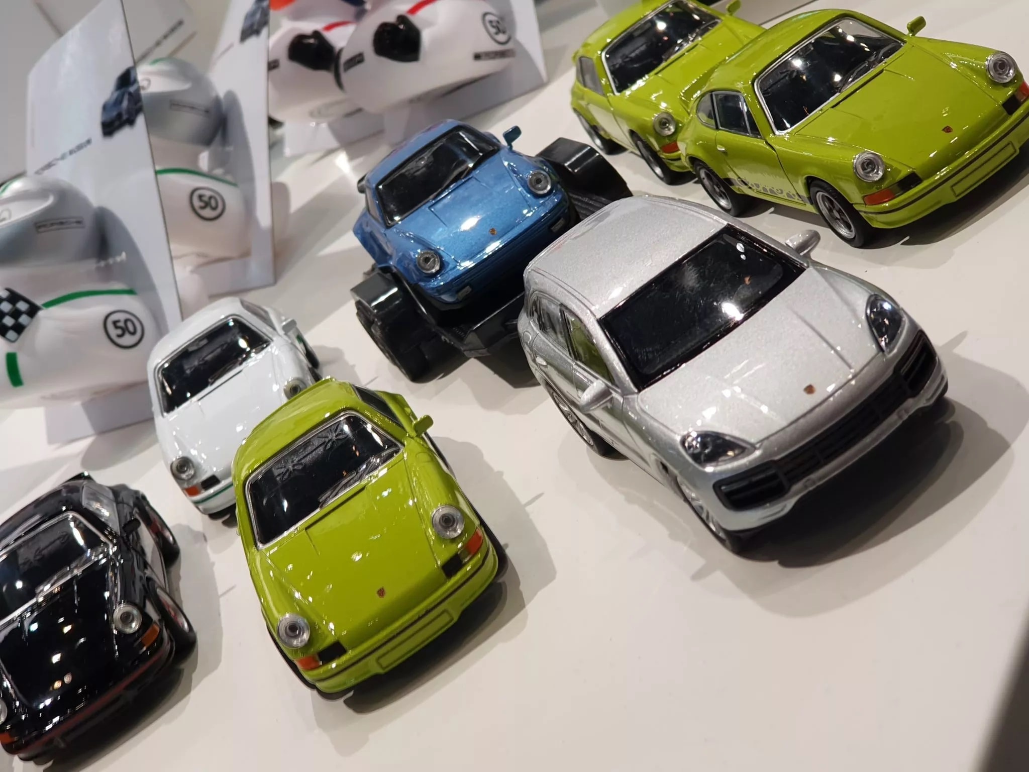 Sammlung von sieben Modellautos, überwiegend Porsche-Modelle in verschiedenen Farben, auf einer Fläche mit Verpackungen im Hintergrund.