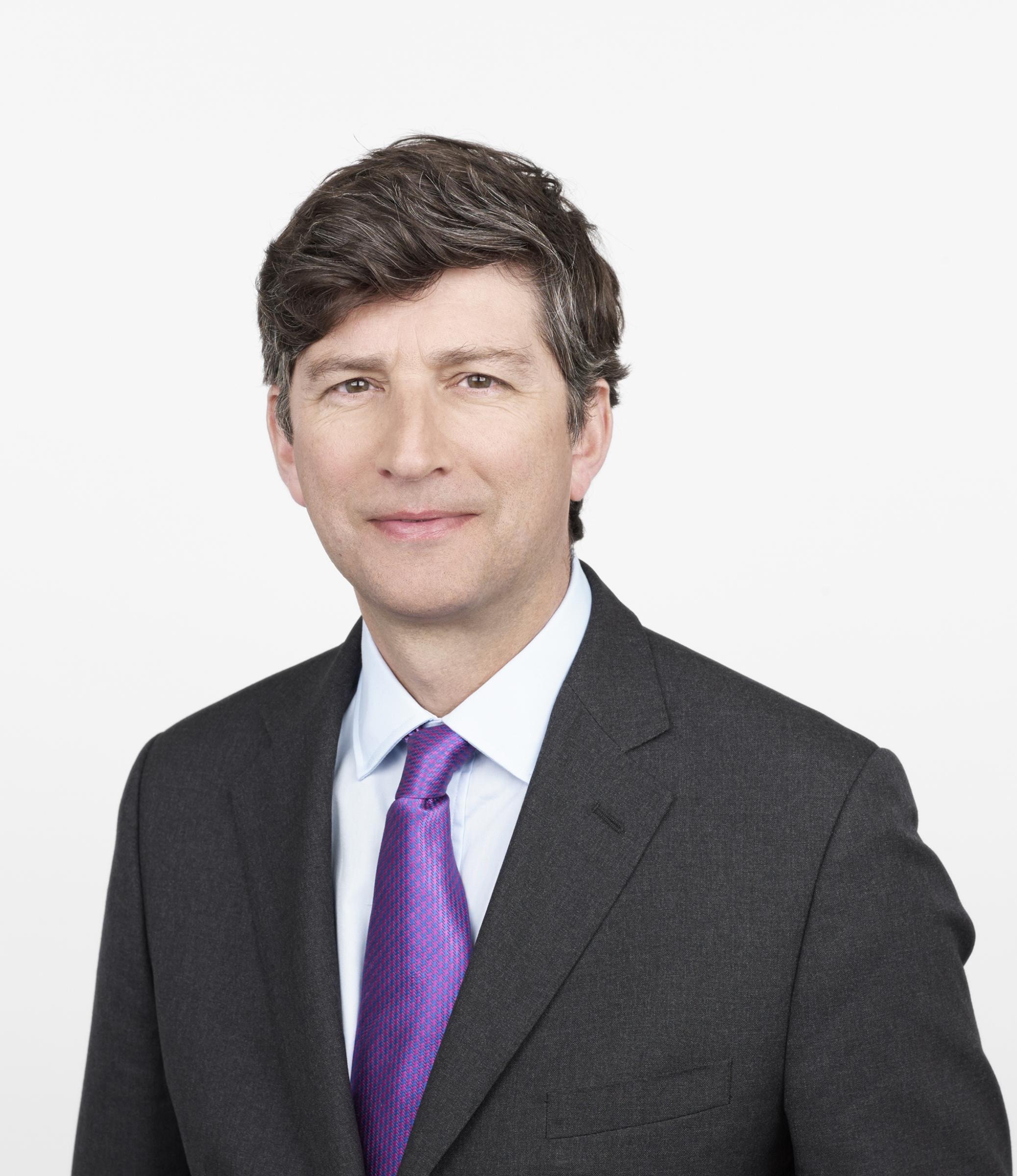 robert read trägt einem dunklen Anzug mit weißem Hemd und lila Krawatte vor weißem Hintergrund.