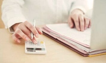 Person bei der Büroarbeit: Berechnungen mit Taschenrechner und Überprüfung von Dokumenten