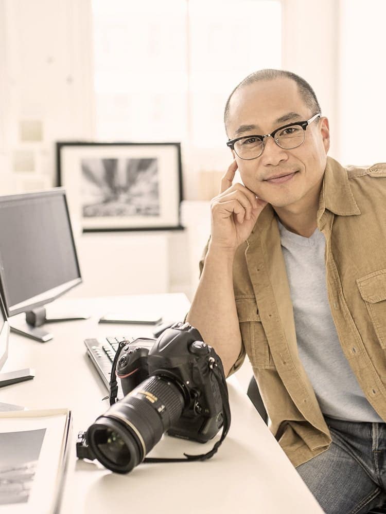 Fotografen-Versicherung von Hiscox: Fotograf sitzt mit seiner Kamera am Schreibtisch