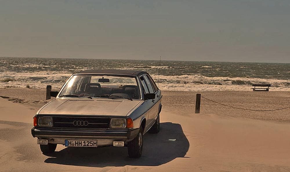 Ein Audi 100 Typ 43 steht am Strand in der Nähe des Meeres geparkt.