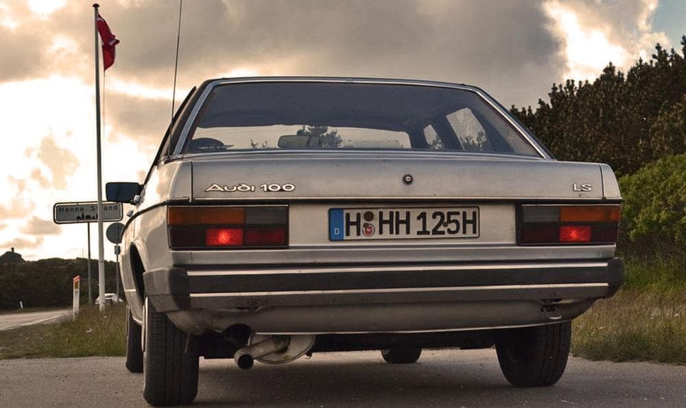Ein parkender Audi 100 Typ 43 am Straßenrand aus der Heckansicht.