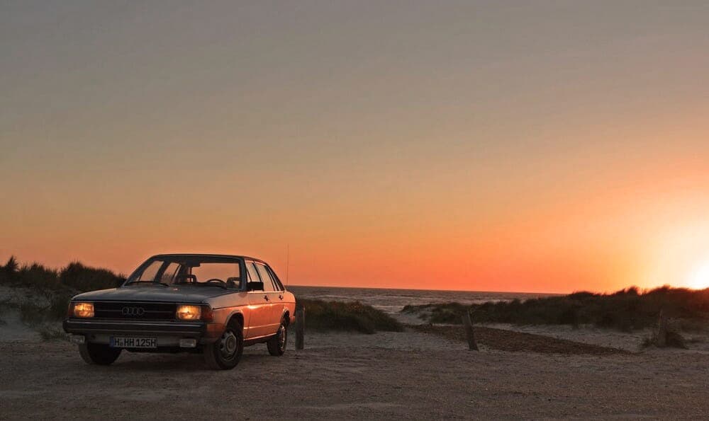 Ein Audi 100 Typ 43, ein Oldtimer, parkt bei Sonnenuntergang am Strand.