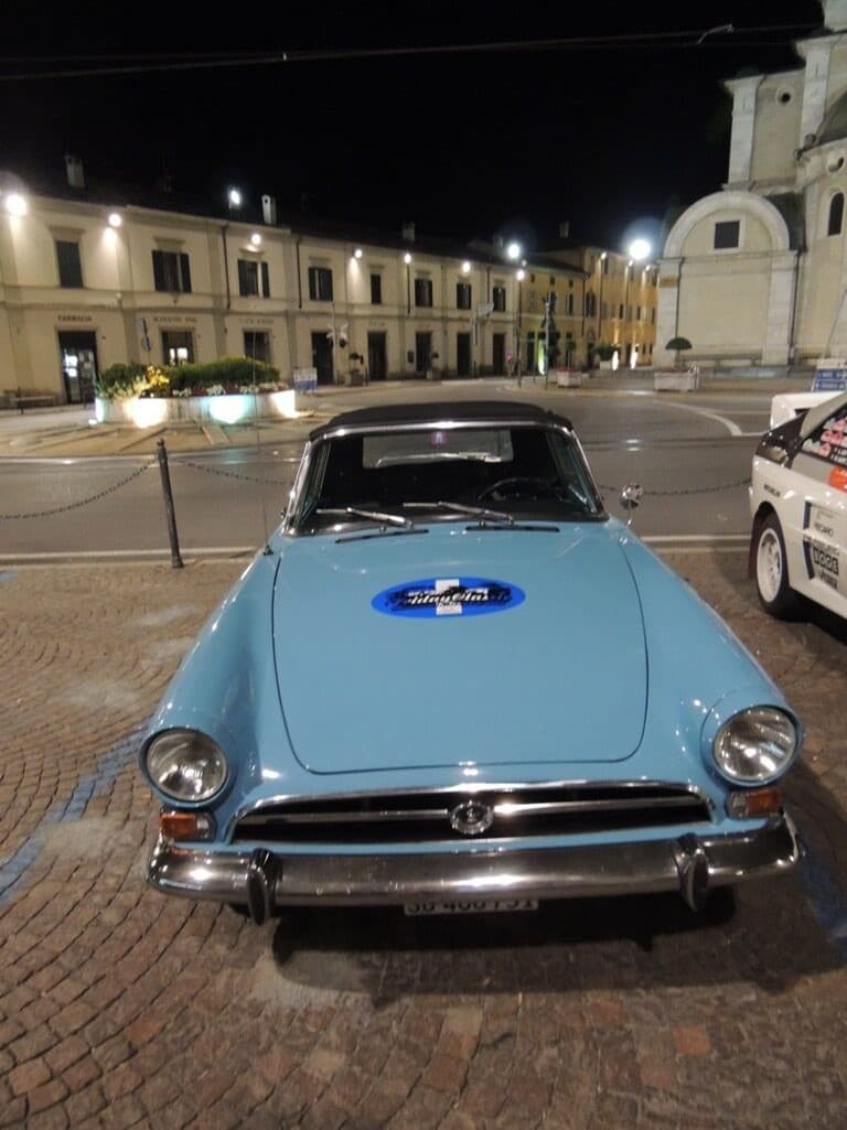 Hellblauer Oldtimer parkt auf einem Kopfsteinpflaster-Gehweg bei Nacht mit einem Aufdruck auf der Motorhaube "Moonwalk Trophy".