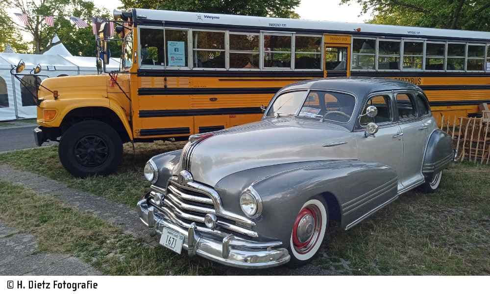 Ein restaurierter 1951 Chevrolet Custom Coupe, der auf einem Pontiac-Chassis basiert, steht neben einem gelben amerikanischen Schulbus.