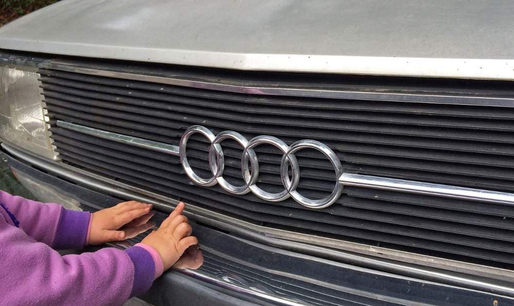 Die Hände eines kleinen Kindes berühren den Kühlergrill eines Audi 100 Typ 43.