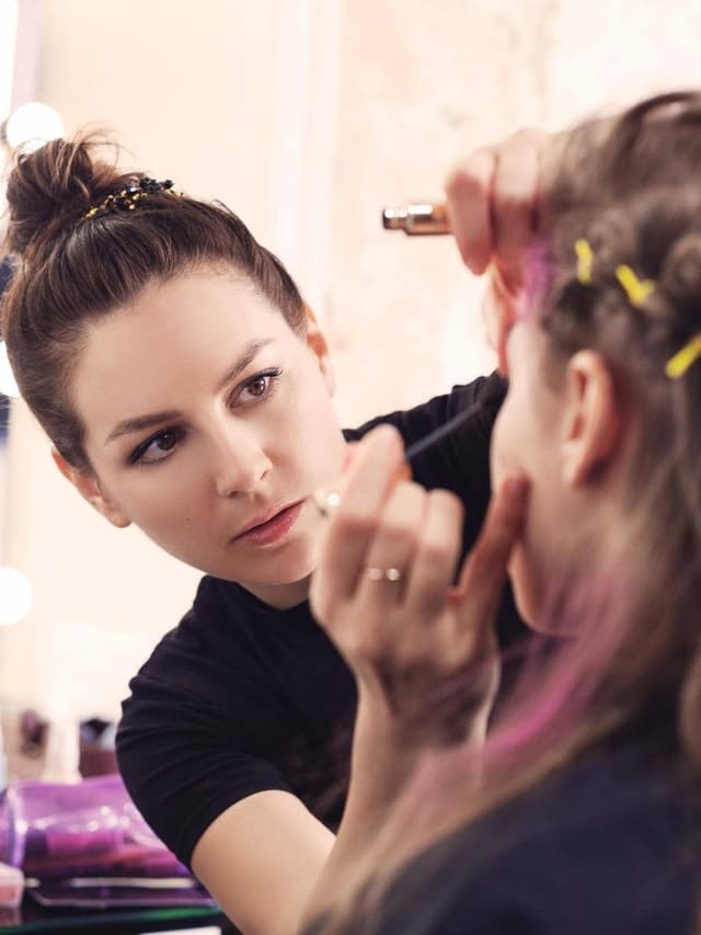 Beauty-Versicherung: Make-Up-Artist mit hochgebundenen Haaren trägt einer Kundin Wimperntusche auf