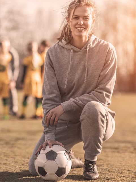 Fußballverein-Versicherung von Hiscox: Junge Fußballtrainerin sitzt vor ihrem Team und blickt in die Kamera