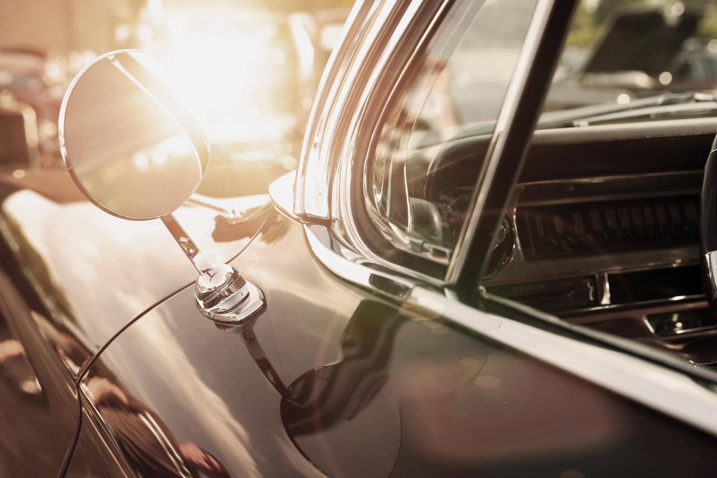 Oldtimer-Versicherung von Hiscox: Nahaufnahme des Seitenspiegels eines klassischen Autos mit spiegelnder Sonne