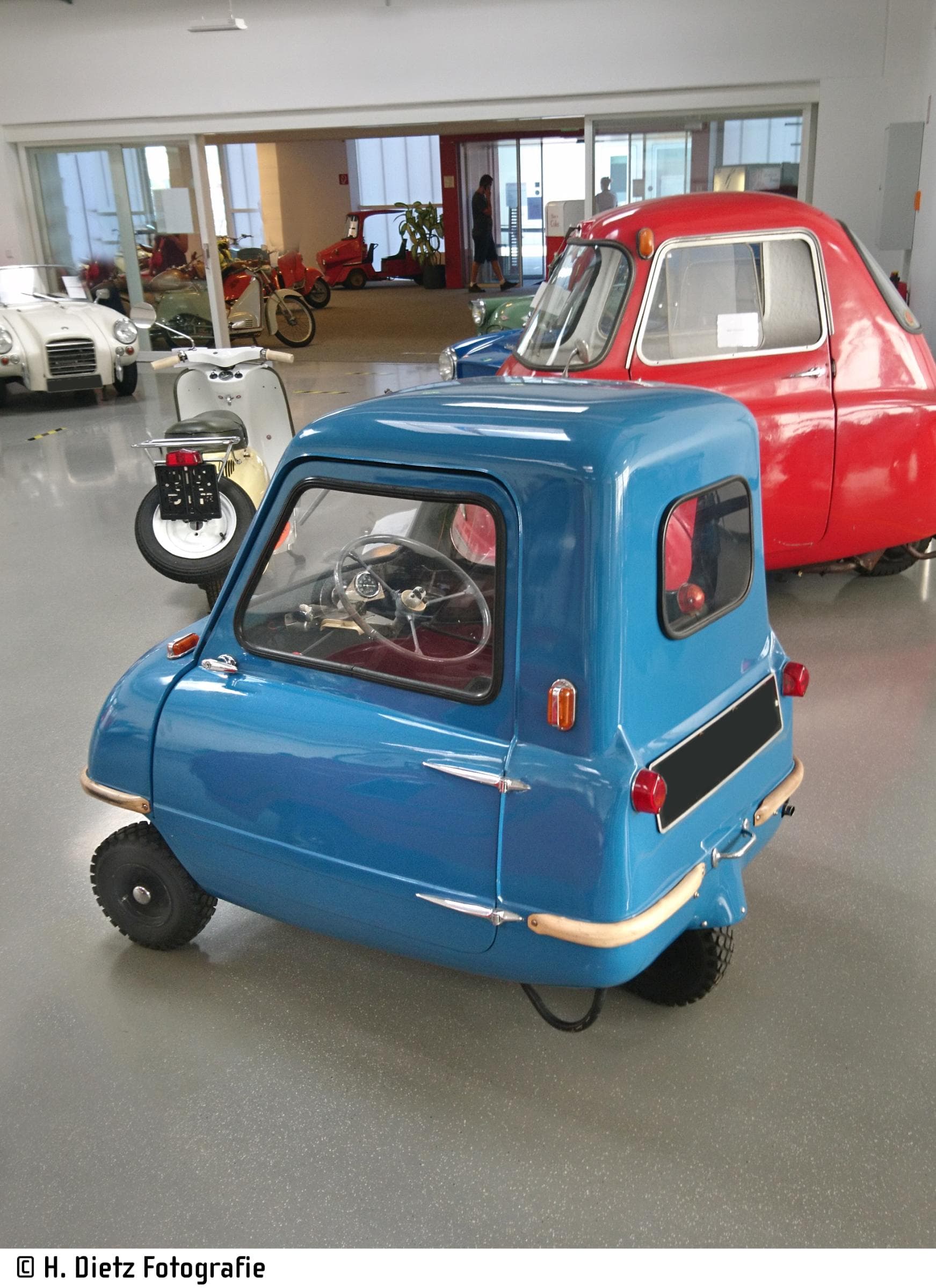 Blauer Peel P50, das kleinste Auto der Welt, parkt in einem Oldtimer-Museum. Man sieht von der Seite in den Fahrzeuginnenraum