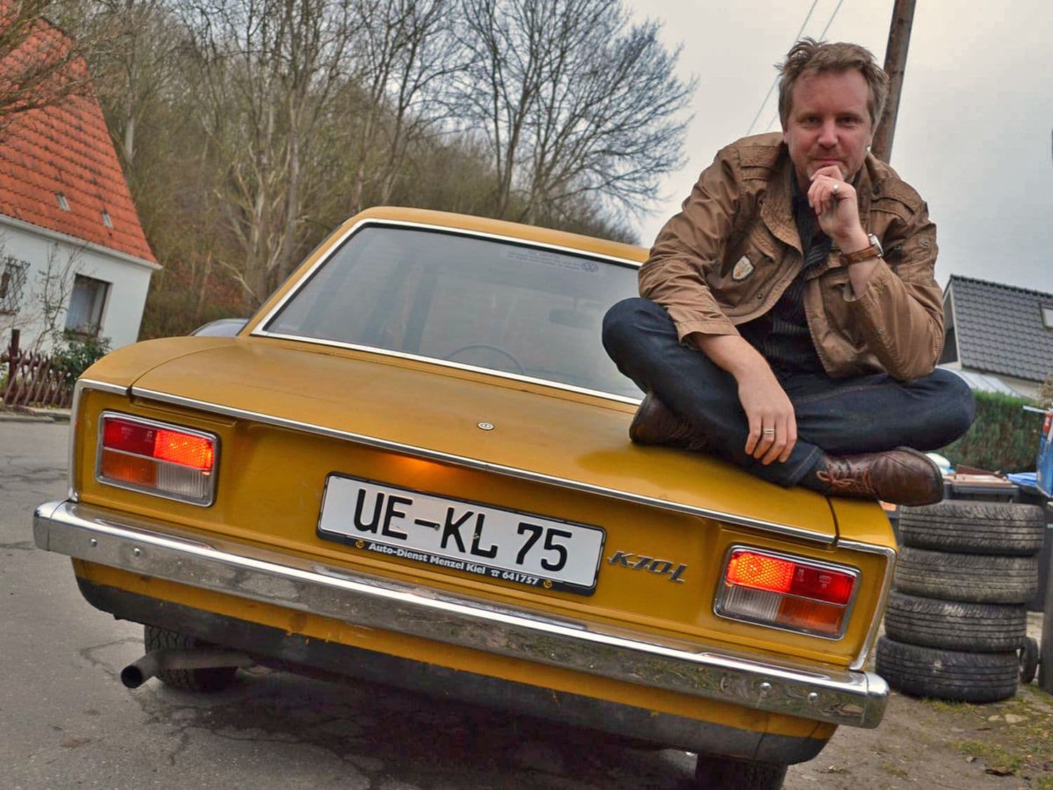 Jens Tanz sitzt auf dem Heck des goldenen Volkswagen Oldtimer K 70 L 1971 im Schneidersitz