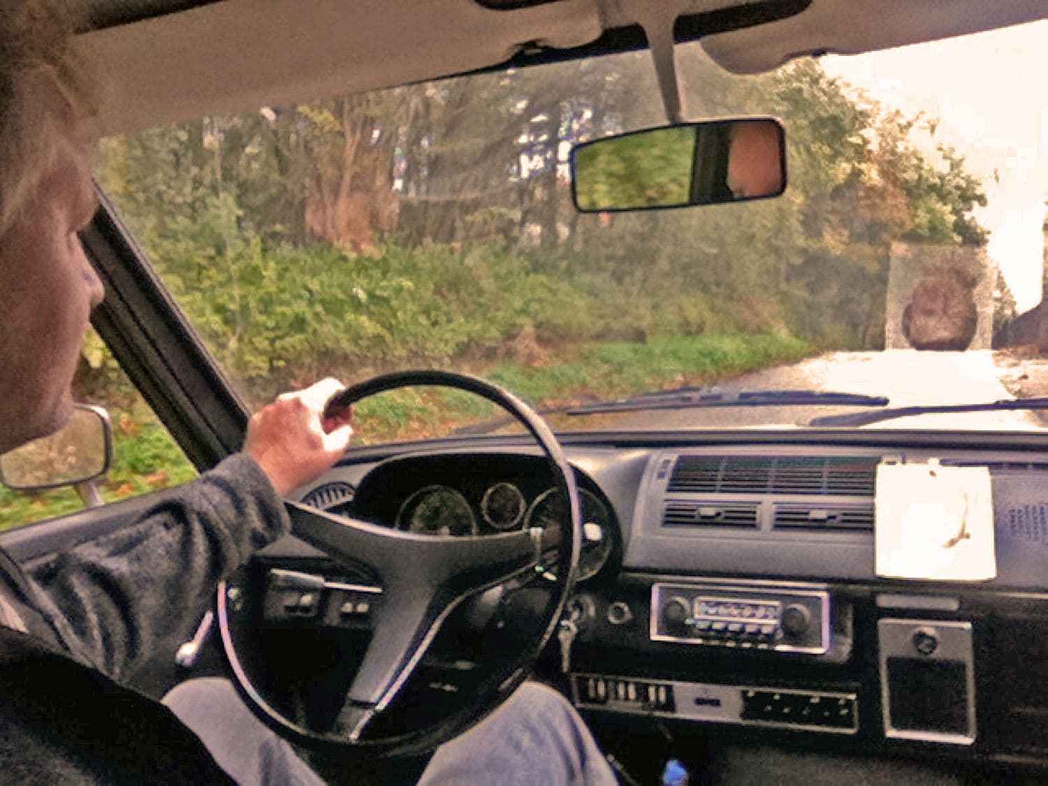 Mann sieht mit einer Hand an dem Lenkrad des VW K70 L 1971 und fährt auf einer Straße